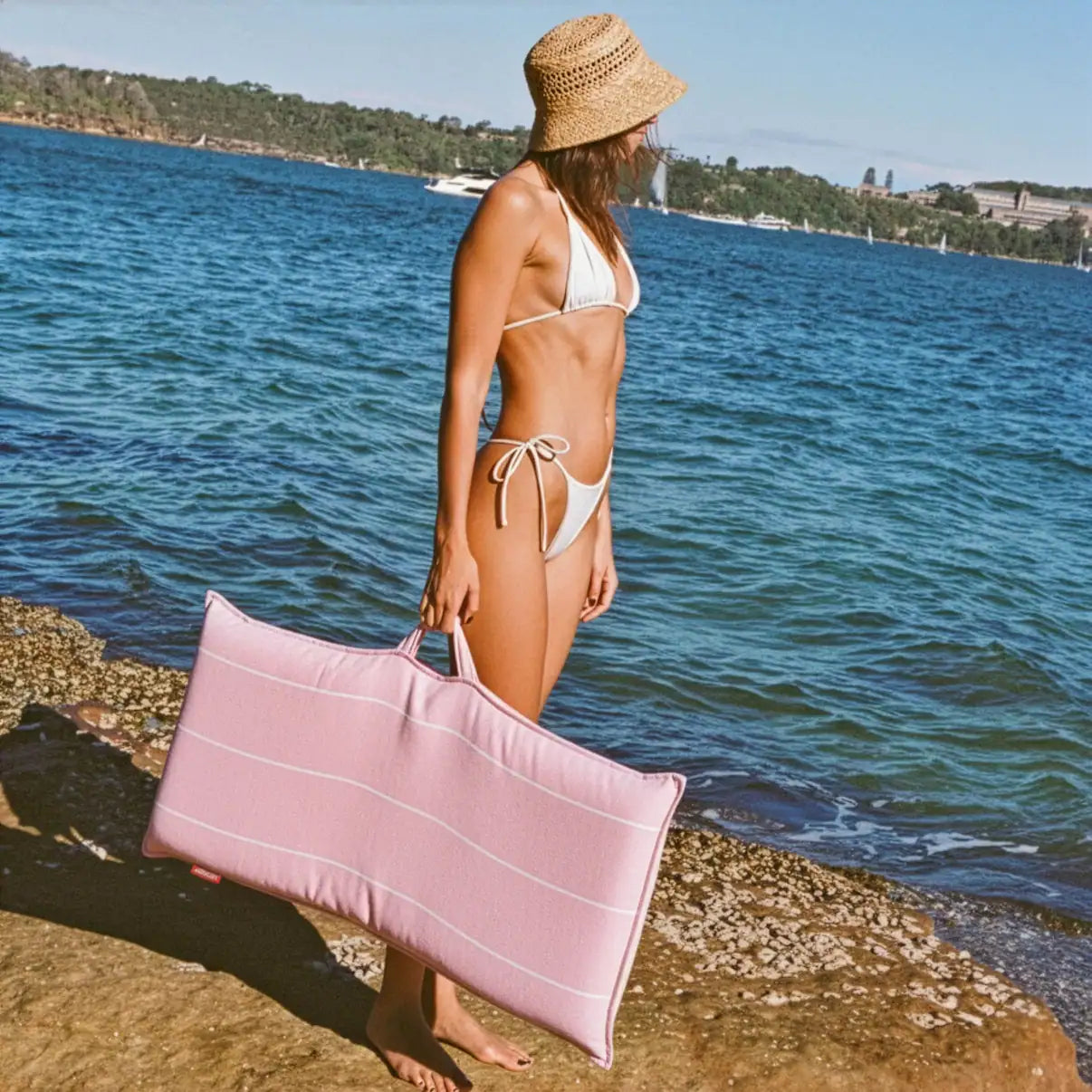 Woman in a bikini carrying a pink La Chaise portable reclining beach lounger by the sea