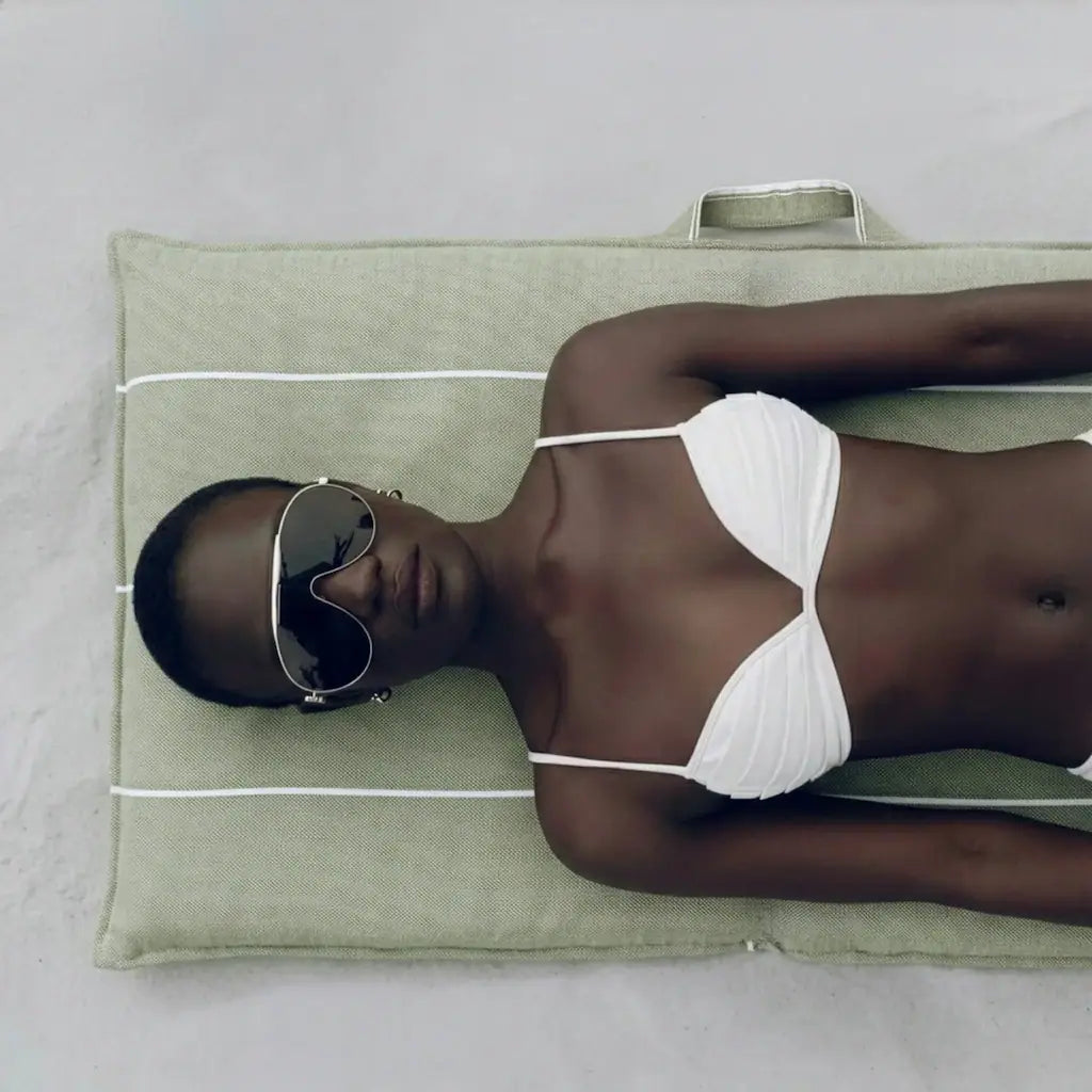 Woman in white bikini lying on a green La Chaise portable reclining beach lounger